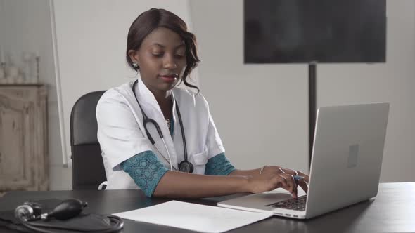 Attractive African Medical Doctor Talking on Telephone Work with Laptop, in Cabinet Hospital, Write