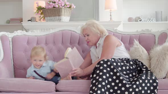 Positive Caucasian Grandmother Reading Book for Little Cute Blond Boy. Bored Child Climbing Down