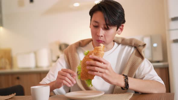 Handsome Asian man eating croissant and drinking coffee