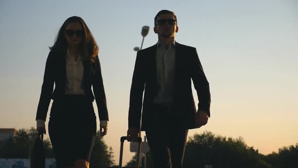 Businessman with His Female Colleague Walking at the City Street and Roll Suitcase on Wheels