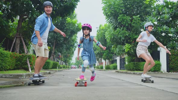 Asian active parents spend leisure time with daughter, enjoy ride Surf Skate Board on street.