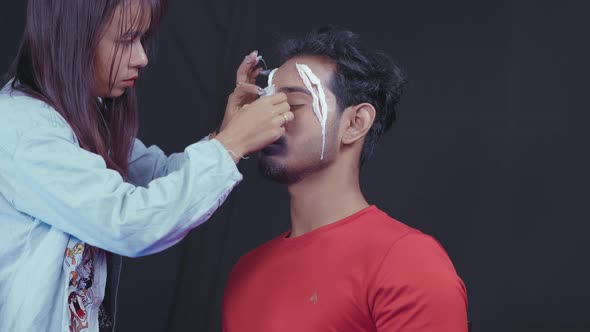 Make up artist putting white prosthetic insert on man's face to make a Halloween mask