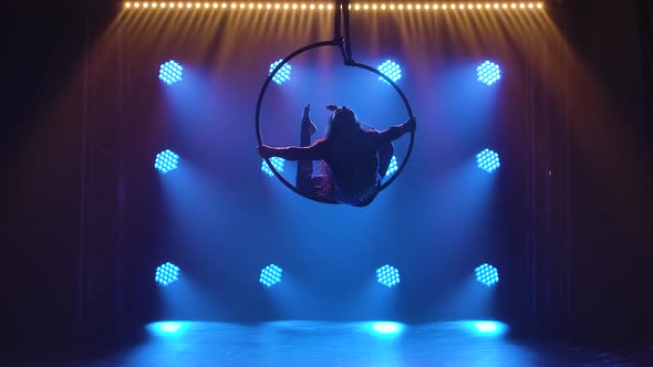 Silhouette Woman Aerialist Performs Acrobatic Elements and Spins in Hanging Aerial Hoop Against