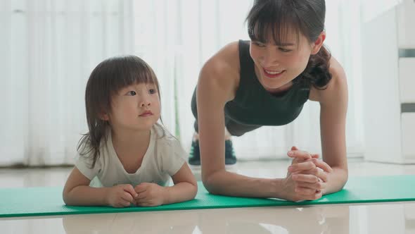 Asian woman exercising yoga works out at home with young little baby playing together around mother.