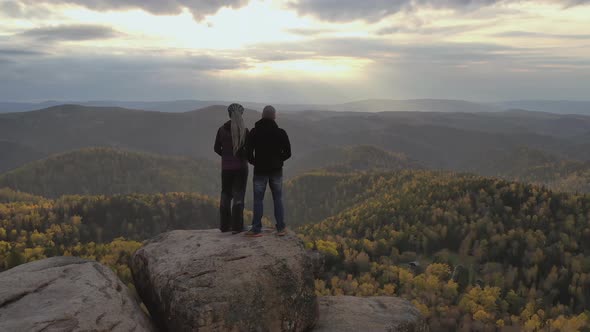 A Young Couple Stand on Top of a Mountain and Enjoy the Sunset. Hikers on a High Cliff. alt
