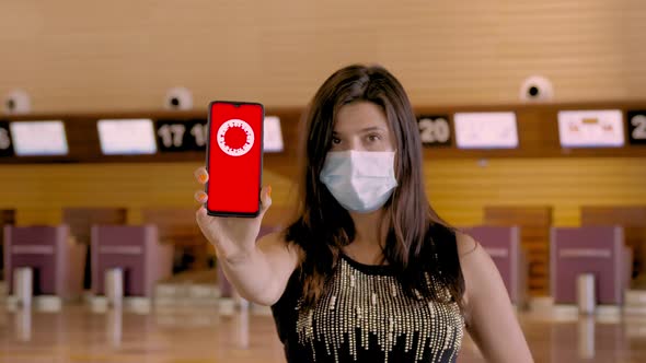 Woman, in Protective Mask, Holds Smartphone with COVID-19 Icon, Text - Stop, on Screen, in Front of