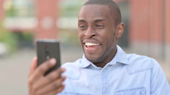 Outdoor Portrait of Excited African Man Celebrating on Smartphone