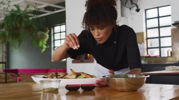 Mixed race female chef preparing a dish and smiling in a kitchen