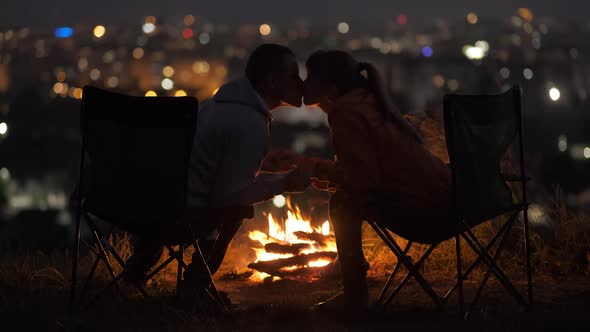 Young Couple in Love Kissing Sitting on Chairs Near Bonfire at Night Enjoying Warm Romantic Evening