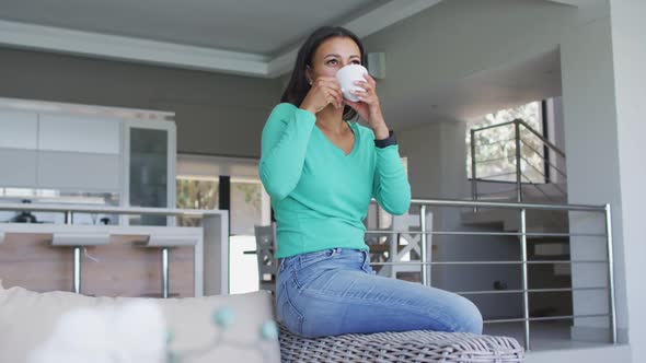 African american woman drinking coffee while sitting on the couch at home