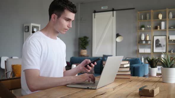 Man Using Phone and Laptop for Work