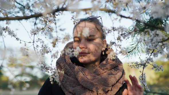 a Beautiful Girl Stands Near a Blossoming Cherry and Looks at the Flowers