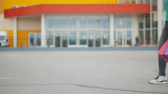 Cropped Shot of Woman Carrying Colorful Paper Bags Walking in Parking Lot After Shopping in Mall