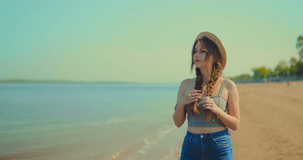 Beautiful Girl in a Hat Walks on the Beach in Summer