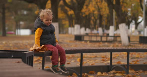 Weekend in Park at Autumn, Little Boy Is Resting on Bench and Smiling, Enjoying Walking at Good Fall