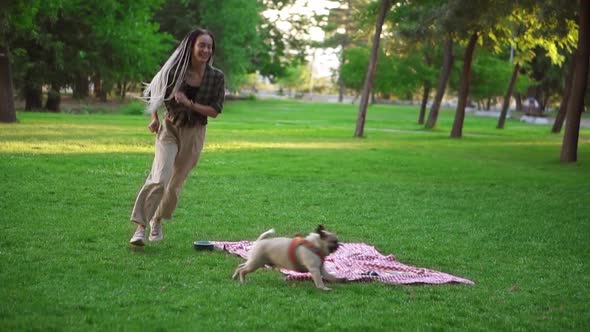 Happy Young Woman Having Fun with Her Dog Outdoors Running Chasing It Around Plaid with Picnic on