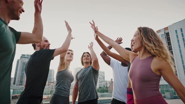 Seven Beautiful Multiracial Friends Giving High Five After Good Workout in the City Streets Outside