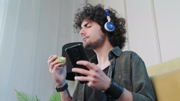 Young Man Listening to the Music and Gesturing While Eatting an Apple