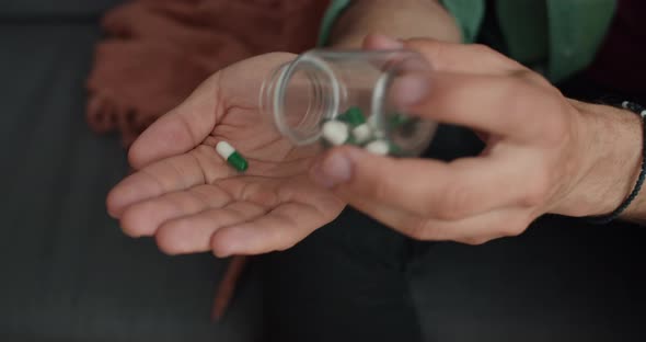 Crop View of Male Person Putting Pills on Hand and Taking Them Wile Sitting on Sofa. Concept of