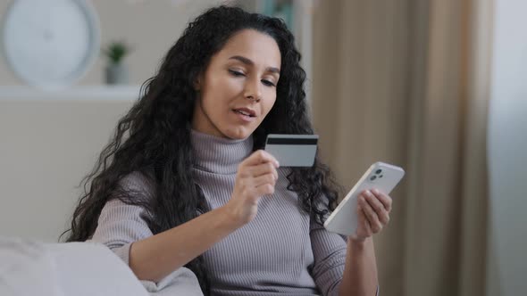 Smiling Young Hispanic Woman Hold Phone and Credit Card Happy Girl Customer Shopping in Online Store