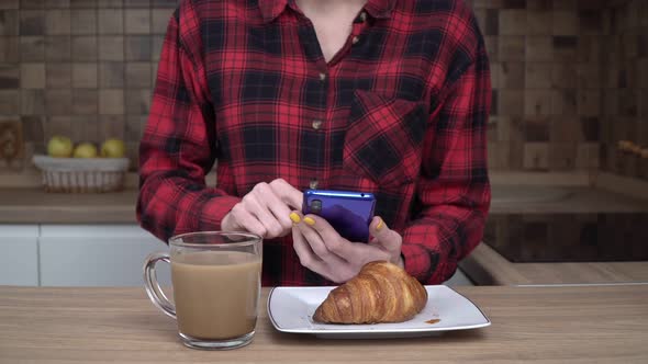 A Young Woman Uses a Smartphone at Home While Having Breakfast