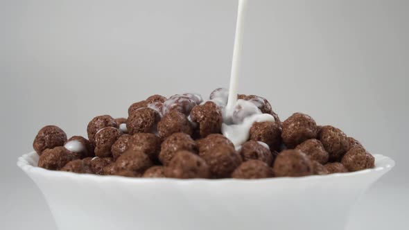 Slow motion pouring milk in white bowl of crunchy cereal chocolate balls flakes