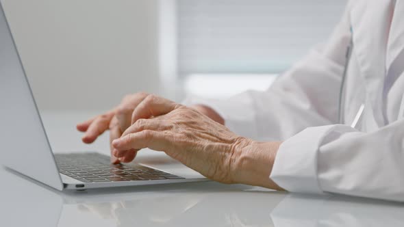 Mature female medical worker types text on laptop