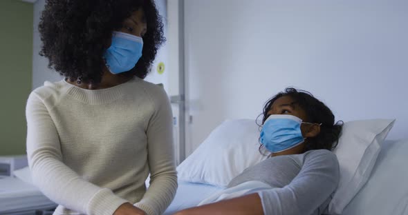 African american mother wearing face mask holding hands and comforting her daughter at hospital
