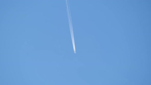 Distant Passenger Jet Plane Flying on High Altitude on Clear Blue Sky Leaving White Smoke Trace of