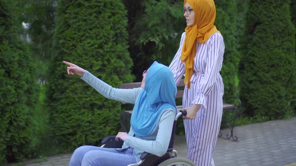 Young Muslim Disabled in a Traditional Scarf and Glasses in a Wheelchair Talking To a Muslim Friend