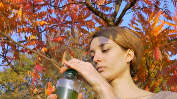 Beautiful Girl Is Drinking Green Drink Spirulina Chlorella and Wheatgrass Smoothie Outdoors in the