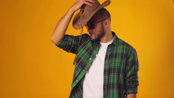 Handsome Young African American Man Putting on Cowboy Hat Against Yellow Background in Studio