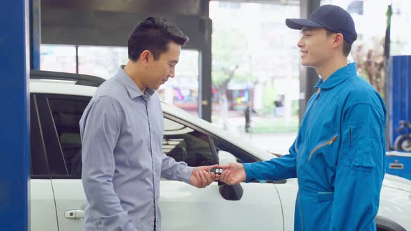 Asian automotive mechanic repairman handing car remote key to client.