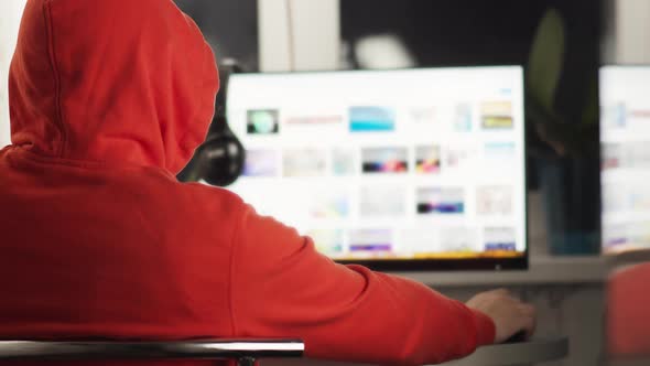 Man in a hood working behind a monitor screen