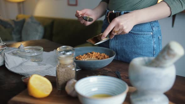 A Young Girl Mixes the Ingredients in a Bowl To Cook Traditional Chickpea Hummus at Home. Close-up