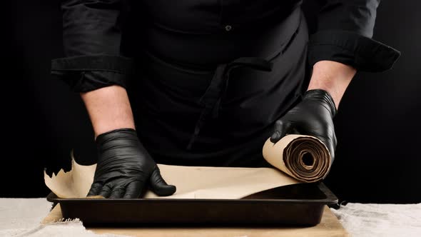 Male chef in black uniform and latex gloves covering a baking shee