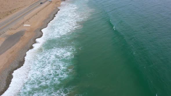 Flying Along Shoreline in Malibu, Aerial Shot Ocean Waves Crashing against Sand, Cars Moving along H