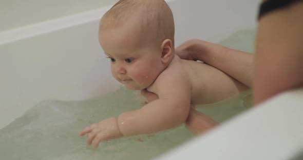 Blueeyed Baby Playing with Water on Mother's Hands in a Bath