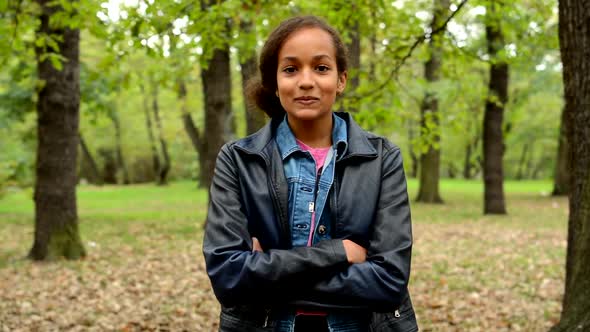 Young African Satisfied Girl Stands with Based Arms in the Park