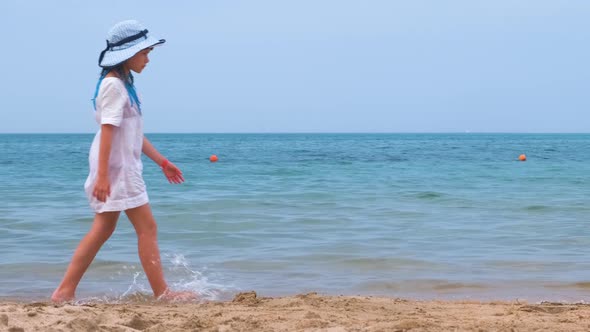 Happy Child Girl in White Summer Dress Walking on Sea Shore Sandy Beach During Summer Vacations