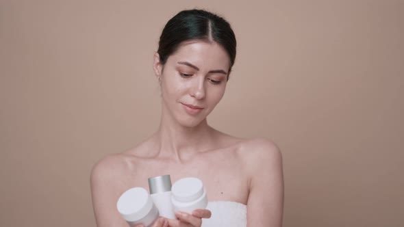 Thoughtful Woman Without Makeup Choosing Cosmetics to Apply on Beige Background