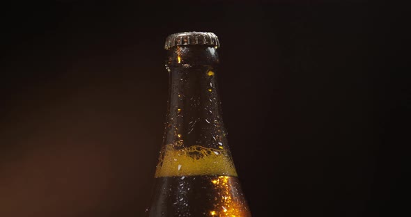 Bottle of Cold Beer on a Black Background. It Slowly Rotates. Condensate