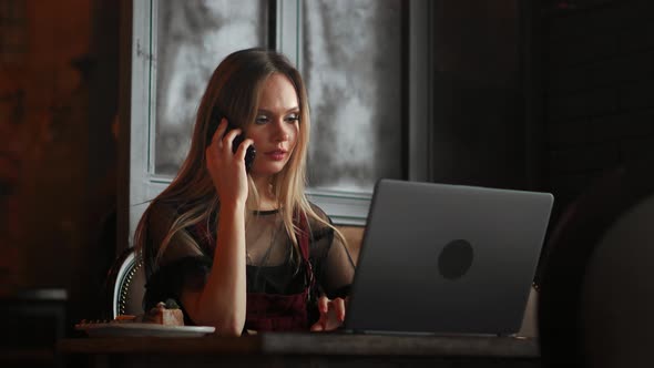 Young Woman Sitting in Coffee Shop at Wooden Table, Drinking Coffee and Using Smartphone