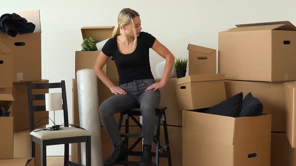 A Moving Woman Sits on a Chair in an Empty Apartment and Acts Irritated, Surrounded By Boxes