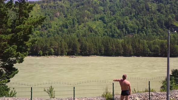Aerial Flying Over a Mountain River with a Rapid Current A Man Dressed in Panties Looks at the River