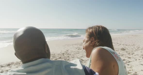 Smiling senior african american couple embracing and looking at sea on sunny beach