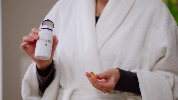 Pedestal Shot of Mature Woman Opening Bottle with Vitamin B Taking Pill Washing Off with Water