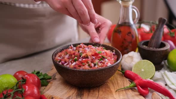 Woman Salting Salsa Dip Sauce in Wooden Bowl at Domestic Kitchen