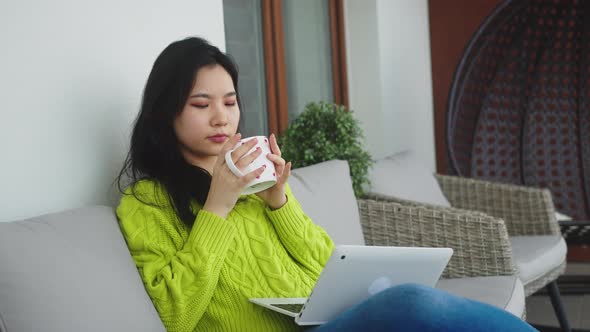 Relaxation and Wellbeing Concept. Young Asian Woman Drinking Cup of Tea While Resting on the Balcony