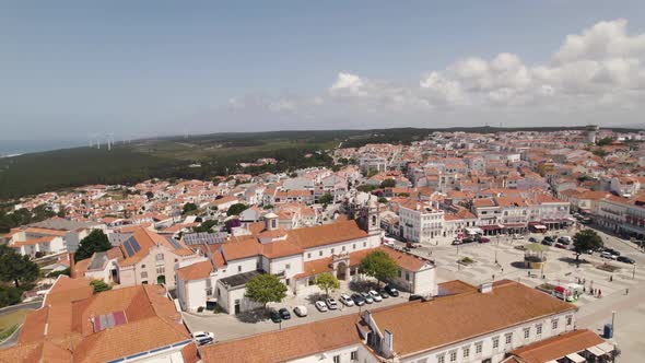 Aerial ascending Sanctuary of Nossa Senhora da Nazaré on the hilltop, rooftops on Cityscape